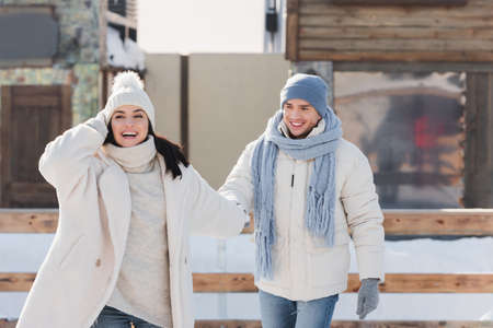 happy young man in winter hat holding hands with girlfriend on ice rinkの写真素材