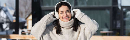 cheerful young woman in sweater and ear muffs in wintertime, bannerの写真素材