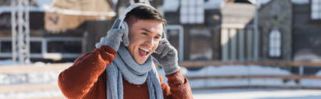 positive young man in sweater and scarf listening music while singing outside, bannerの写真素材