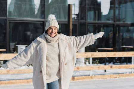 pleased young woman in winter hat and coat skating on ice rinkの写真素材
