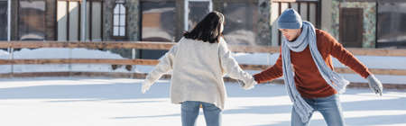 young woman in ear muffs holding hands with boyfriend on ice rink, bannerの写真素材