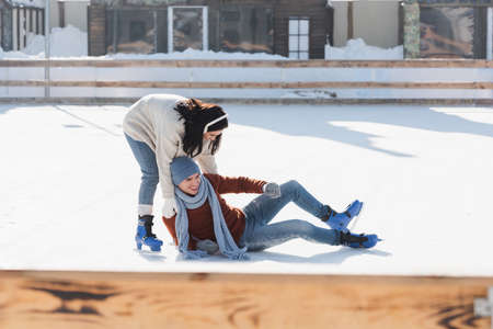 full length of happy man falling near woman while skating on ice rink outsideの写真素材