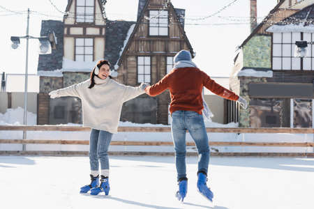 full length of positive young woman in ear muffs holding hands with boyfriend on ice rinkの写真素材