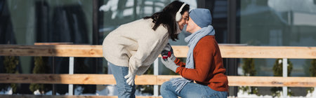happy man holding box with wedding ring and kneeling while making proposal to woman on ice rink, bannerの写真素材