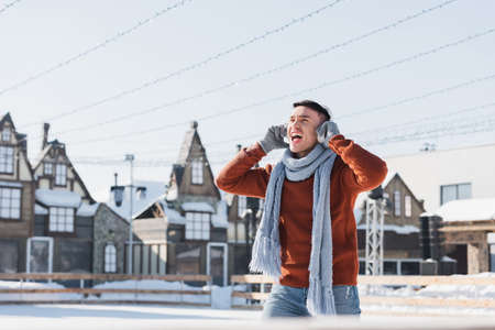 positive young man in sweater and scarf listening music while singing outsideの写真素材