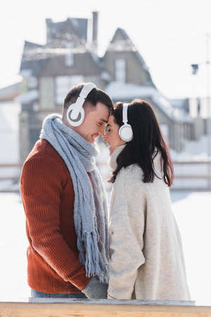 side view of smiling couple hugging while listening music in headphones outsideの写真素材