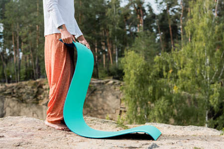 cropped view of barefoot buddhist holding yoga mat on rocky cliff in forestの写真素材
