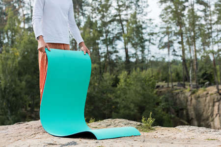 partial view of buddhist holding yoga mat on rocky cliff in forestの写真素材