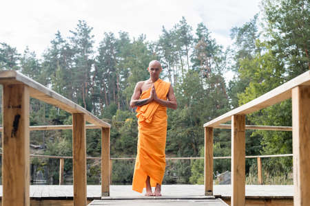 full length view of buddhist monk praying on wooden platform in forestの写真素材
