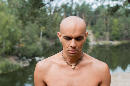 shirtless buddhist in beads meditating with closed eyes in forestの写真素材
