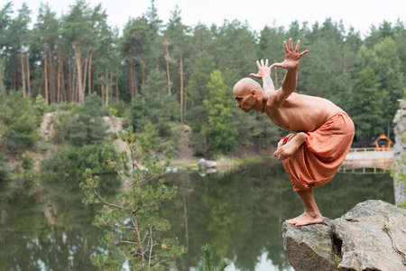 shirtless buddhist meditating in yoga pose with outstretched hands on rocky cliff over riverの写真素材
