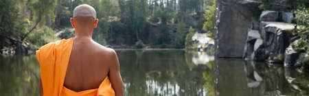 back view of buddhist monk meditating near forest pond, bannerの写真素材
