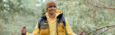 happy man with trekking poles looking away in forest, bannerの写真素材