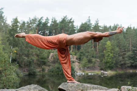 side view of shirtless buddhist meditating in half moon pose on rocks over riverの写真素材
