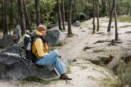 hiker with backpack sitting on stone in forest and looking awayの写真素材