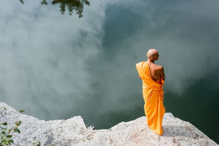high angle view of buddhist monk meditating on rocky cliff over waterの写真素材