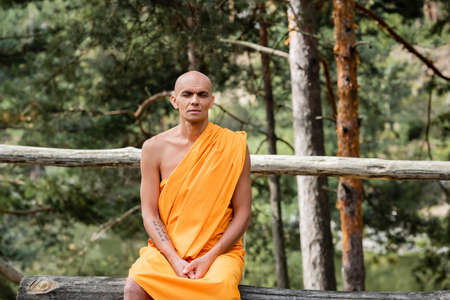buddhist sitting on log bench and meditating with closed eyes in forestの写真素材