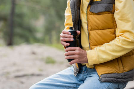 cropped view of tourist in warm vest opening thermo bottle outdoorsの写真素材