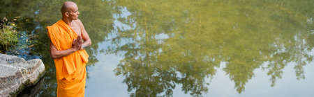 high angle view of buddhist monk looking at lake while meditating with praying hands, bannerの写真素材