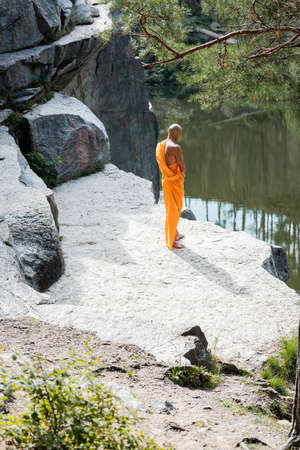 high angle view of buddhist monk meditating near rocks over forest lakeの写真素材