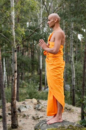 side view of barefoot buddhist in orange kasaya praying in forestの写真素材