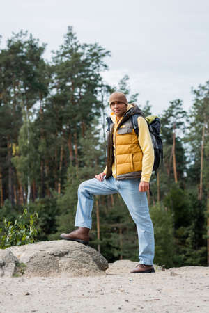 hiker in warm vest and beanie standing on rocky hill and looking at cameraの写真素材