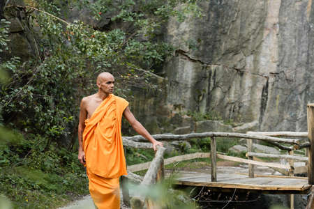 man in traditional buddhist robe walking near wooden fence in forestの写真素材