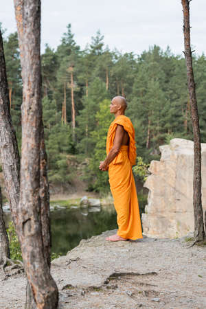full length view of buddhist monk meditating on rocky cliff in forestの写真素材