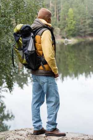 hiker in warm west and jeans looking at lake in autumn forestの写真素材
