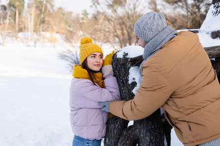 Young woman looking at boyfriend in winter outfit near tree in parkの写真素材