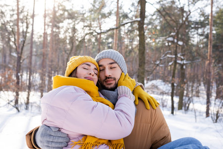 Young couple in winter clothes hugging with closed eyes in park