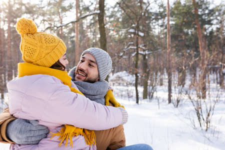 Smiling man hugging girlfriend in knitted hat in winter parkの写真素材