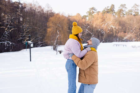 Side view of smiling man lifting girlfriend in park with snowの写真素材