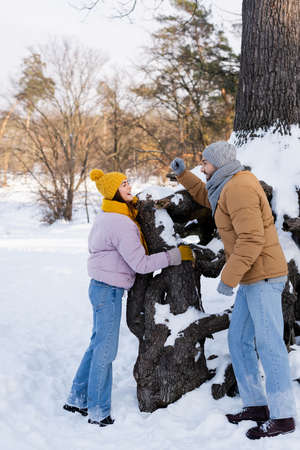 Side view of smiling woman standing near tree with snow and boyfriend in parkの写真素材