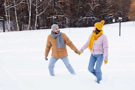 Smiling couple holding hands while walking on snow in parkの写真素材