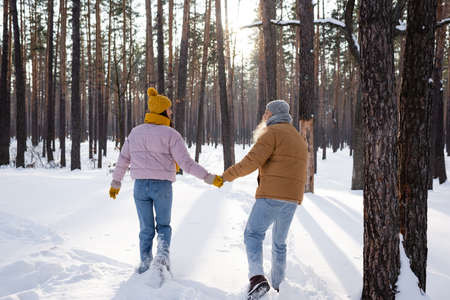 Side view of young couple holding hands in gloves while walking in snowy parkの写真素材