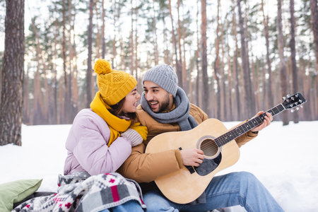 Happy couple playing acoustic guitar on snow in winter parkの写真素材
