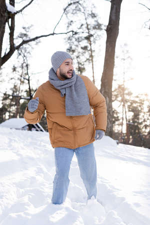 Positive man in hat and scarf looking away in snow outdoorsの写真素材