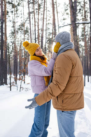 Pretty woman smiling while touching face of boyfriend in winter park