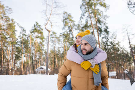 Smiling woman piggybacking on boyfriend in winter parkの写真素材