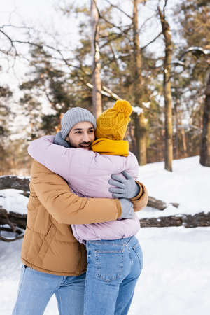 Smiling man hugging girlfriend in winter outfit in park at daytimeの写真素材