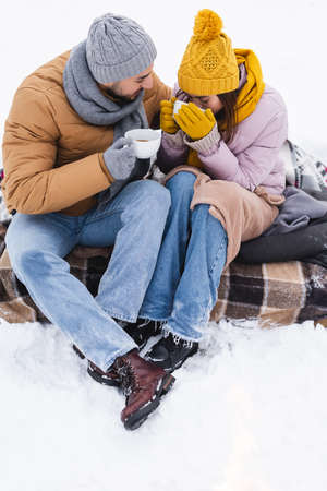 Young woman drinking coffee near boyfriend in snowy parkの写真素材