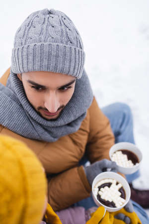 Overhead view of man looking at girlfriend while holding cup of cacao in winter parkの写真素材