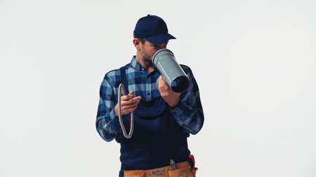 Handyman in overalls looking at plastic pipe isolated on whiteの写真素材