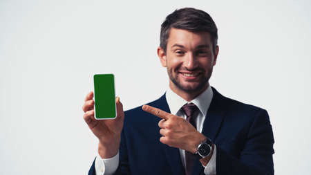 Smartphone with green screen in hand of blurred businessman pointing with finger isolated on whiteの写真素材