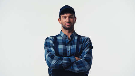 Workman in cap and overalls standing with crossed arms isolated on whiteの写真素材