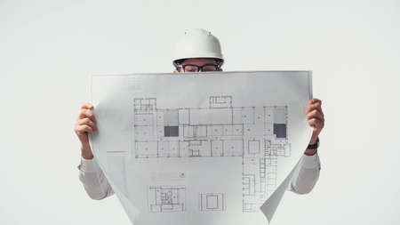 Engineer in hardhat covering face with blueprint isolated on whiteの写真素材