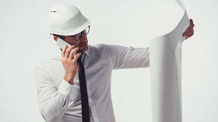 Architect in hardhat talking on smartphone and looking at blueprint isolated on white