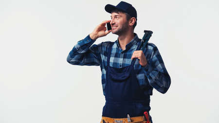 Positive workman with pipe wrench talking on smartphone isolated on whiteの写真素材