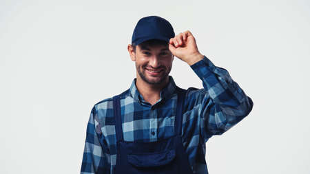 Happy workman adjusting cap and looking at camera isolated on whiteの写真素材